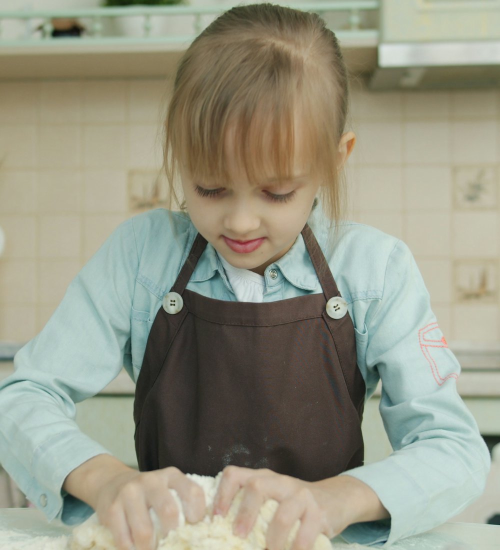 A girl in an apron kneading dough in a kitchen