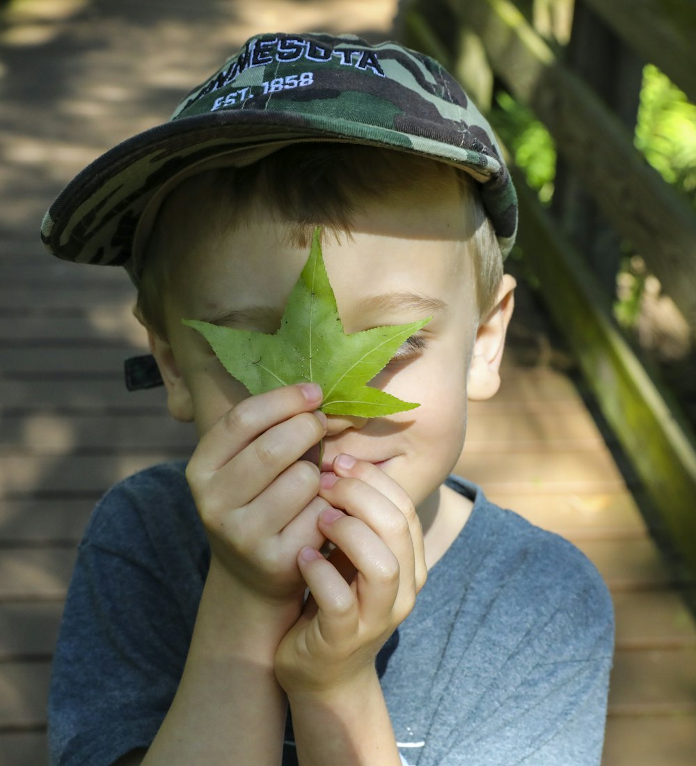 A boy holding a green leaf up to his face on a wooded boardwalk